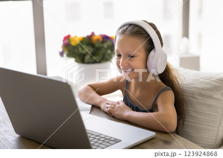 Little girl listens audio lesson through headphones, e-learning using laptop Little girl listens audio lesson through headphones, e-learning using laptop 123924868