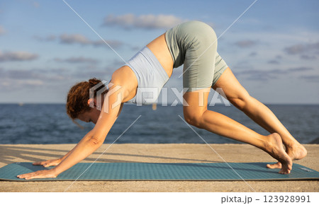 Yoga practice on embankment, female athlete fulfil carry out Adho Mukha Svanasana 123928991