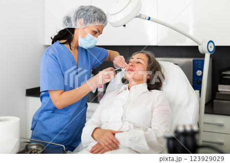 Cosmetologist giving beauty injections to elderly female client Cosmetologist giving beauty injections to elderly female client 123929029