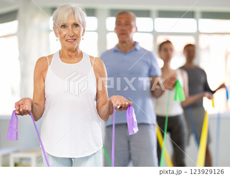 Elderly woman during Pilates strength training standing performs exercises resistance band 123929126