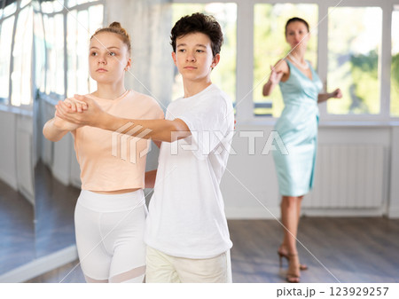 Dance lesson - teacher teaches teenage girl and boy to dance tango in studio Dance lesson - teacher teaches teenage girl and boy to dance tango in studio 123929257