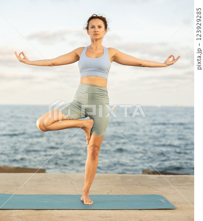 Athletic female yoga practitioner performing Garudasana on beach Athletic female yoga practitioner performing Garudasana on beach 123929285