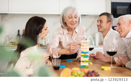 Group of mature spouses and son with girlfriend is playing board game with wooden blocks in kitchen Group of mature spouses and son with girlfriend is playing board game with wooden blocks in kitchen 123929313