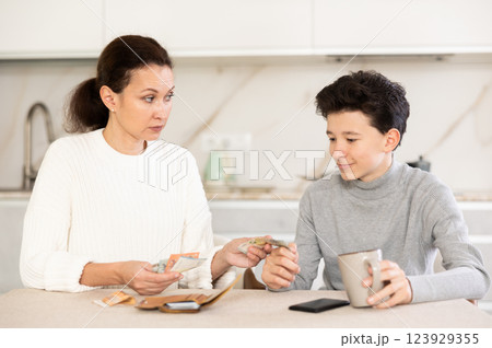 Mother giving some cash and instructions her teenager son sitting at home Mother giving some cash and instructions her teenager son sitting at home 123929355