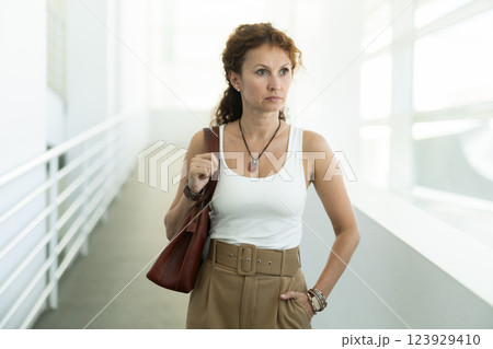 Woman in forties with handbag walking through bright corridor 123929410
