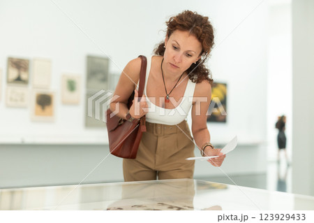 Middle-aged woman looking at objects under showcase in museum 123929433
