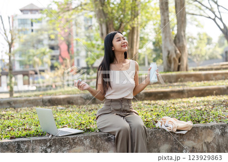 Sustainable lifestyle. Joyful young woman savoring a drink while sitting in a peaceful park. 123929863
