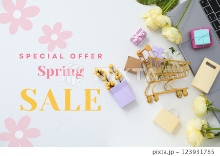 Hello spring, laptop, shopping cart figurine, gift boxes and flowers on a light background, top view, with text 123931785