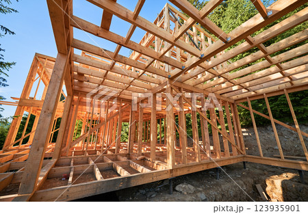 Housing wooden-frame house built near woodland area. Start of novel construction of comfortable cottage on edge of the forest. Concept of contemporary ecological construction and modern architecture. Housing wooden-frame house built near woodland area. Start of novel construction of comfortable cottage on edge of the forest. Concept of contemporary ecological construction and modern architecture. 123935901