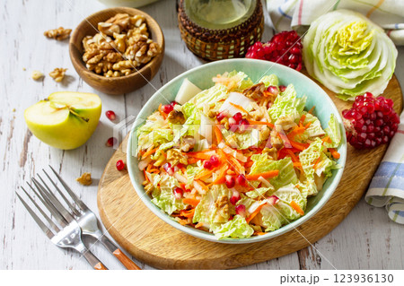 Dietary salad fresh vegetable of Chinese cabbage, carrots, apple, nuts and pomegranate with vinaigrette dressing on a white wooden table. 123936130