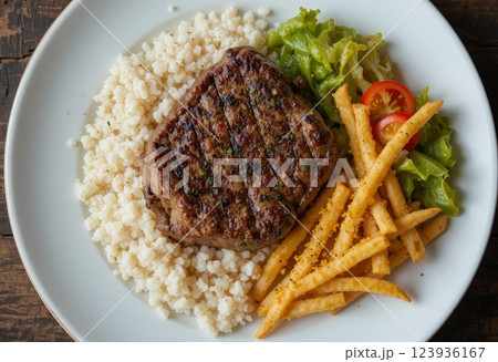 Dish with rice, whole steak meat, French fries, green lettuce and tomato slices. Dish with rice, whole steak meat, French fries, green lettuce and tomato slices. 123936167