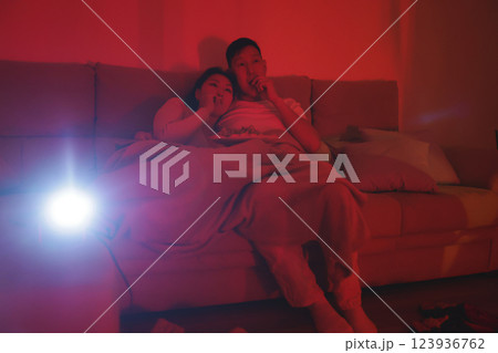 Young couple watching movie using projector at home and eating snacks 123936762