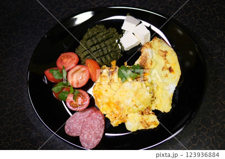 omelette sausage tomatoes pasta pesto and feta on plate breakfast lunch black dishes 123936884