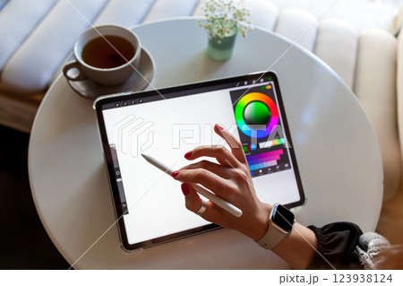 A girl in a cafe draws with a stylus on a graphics tablet. 123938124