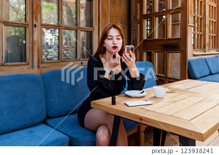 A girl in a cafe at a table paints her lips with red lipstick 123938241