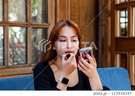 A girl in a cafe at a table paints her lips with red lipstick 123938347