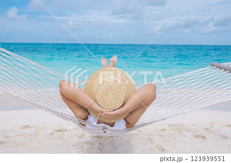 A young woman in a straw hat has her hands behind her head and is lying in a hammock near the ocean A young woman in a straw hat has her hands behind her head and is lying in a hammock near the ocean 123939551