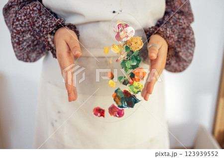 Close-up of well-groomed female hands holding plastic palette with mixed colors Close-up of well-groomed female hands holding plastic palette with mixed colors 123939552