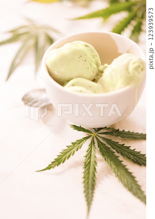 A hemp leaf is lying on a mock-up jars of ice cream on a white marble table 123939573
