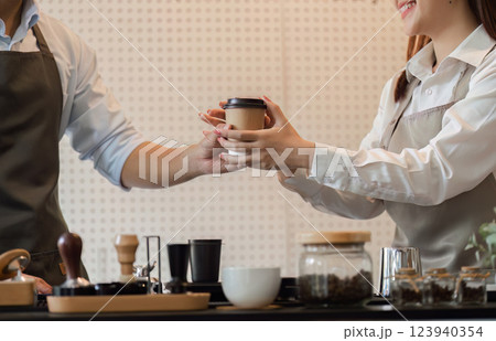 Customer Service and Sustainable Coffee. A barista hands a freshly prepared coffee to a customer with a smile. Customer Service and Sustainable Coffee. A barista hands a freshly prepared coffee to a customer with a smile. 123940354
