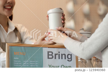 Creating Awareness in Sustainable Choices. A customer hands over their own cup to the barista in a friendly cafe environment. 123940360