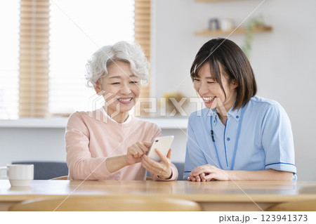 スマートフォンを持ったシニア女性と話をする介護スタッフ スマートフォンを持ったシニア女性と話をする介護スタッフ 123941373