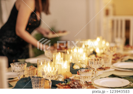 A beautiful young woman in a black evening dress sets the festive table. A beautiful young woman in a black evening dress sets the festive table. 123943583