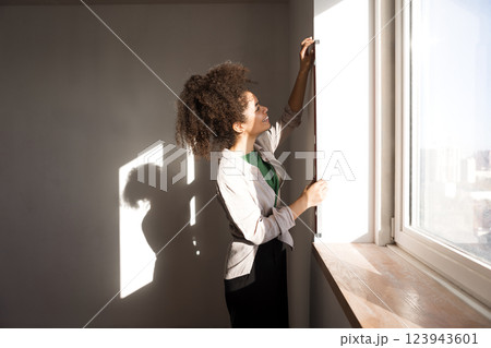 A young charming girl of mixed race measures the level of the window opening. Renovation in a house or apartment. 123943601