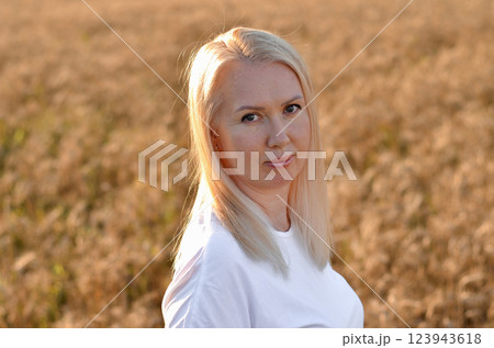 Woman stands in a golden field of wheat during sunset, showcasing natural beauty and serenity in a rural setting 123943618