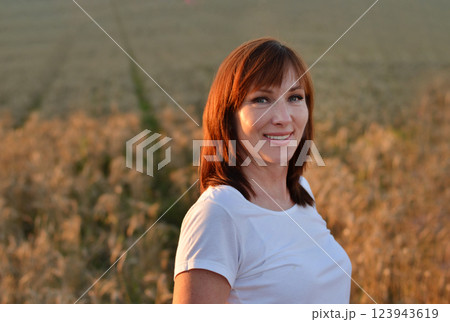 Woman with long hair in pink dress stands in golden wheat field during sunset, highlighting natural beauty and serene landscape Woman with long hair in pink dress stands in golden wheat field during sunset, highlighting natural beauty and serene landscape 123943619