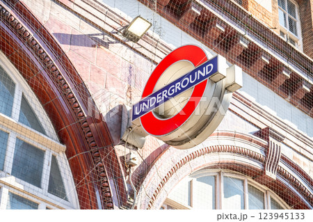 A prominent Underground sign stands out against the architectural backdrop in England. This sign is a recognizable feature of the public transport system in London, attracting travelers daily. 123945133