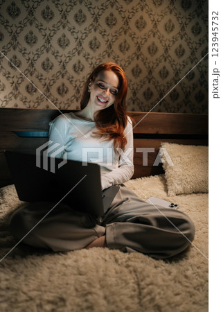Vertical portrait of successful female freelancer typing on laptop smiling looking to screen sitting comfortably in bed, working remotely in cozy bedroom late at night. Concept of modern lifestyle. Vertical portrait of successful female freelancer typing on laptop smiling looking to screen sitting comfortably in bed, working remotely in cozy bedroom late at night. Concept of modern lifestyle. 123945732