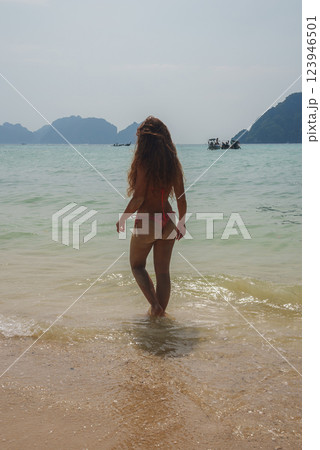 A woman with long hair stands on a sandy beach in Koh Phi Phi, Thailand, facing turquoise waters with limestone cliffs, islands, and boats in the distance. A woman with long hair stands on a sandy beach in Koh Phi Phi, Thailand, facing turquoise waters with limestone cliffs, islands, and boats in the distance. 123946501