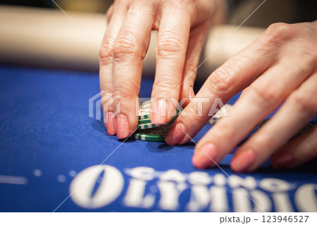 Close up of hands with pink glittery nail polish stacking green poker chips on a blue felt table with Casino Olympic text partially visible. Close up of hands with pink glittery nail polish stacking green poker chips on a blue felt table with Casino Olympic text partially visible. 123946527