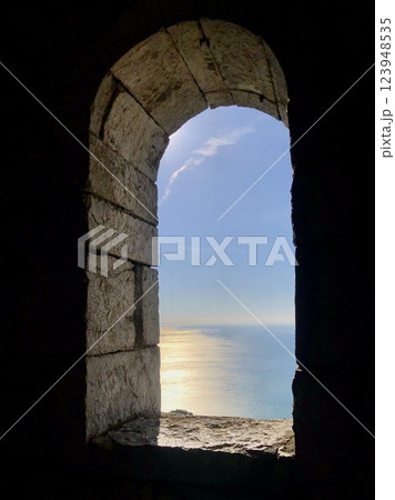Sea view through the oval window of the stone tower. Sea surface illuminated by the evening sun. Sea view through the oval window of the stone tower. Sea surface illuminated by the evening sun. 123948535