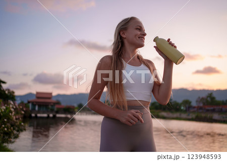 A fitness enthusiast enjoys refreshment and hydration while basking in the sunsets glow 123948593