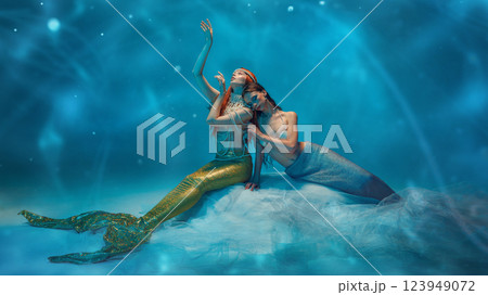 Tender and graceful young women dressed in mermaid glowing tails and pearl accessories, sitting on vail with dreamy like expression 123949072