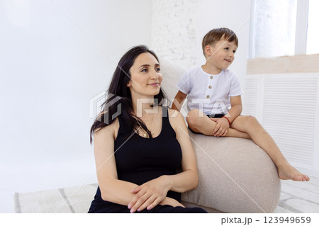 A young pregnant woman in a black dress is sitting with her son on the couch. Adorable mom and her little boy on the sofa. A young pregnant woman in a black dress is sitting with her son on the couch. Adorable mom and her little boy on the sofa. 123949659