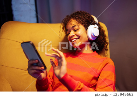 Smiling African woman is sitting in armchair and using phone Smiling African woman is sitting in armchair and using phone 123949662