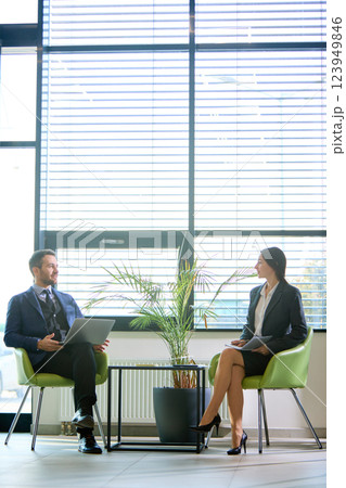 Two professionals in formal attire engaging in discussion with relaxed atmosphere in modern business lounge. Two professionals in formal attire engaging in discussion with relaxed atmosphere in modern business lounge. 123949846
