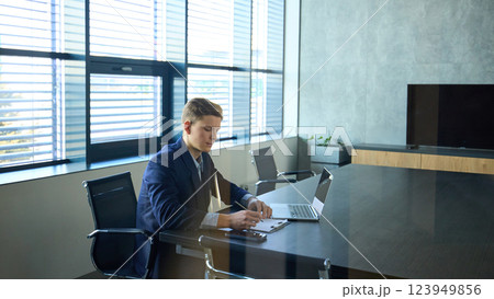 Young professional in navy blue suit working on laptop in quiet modern office, reflecting diligence and ambition 123949856