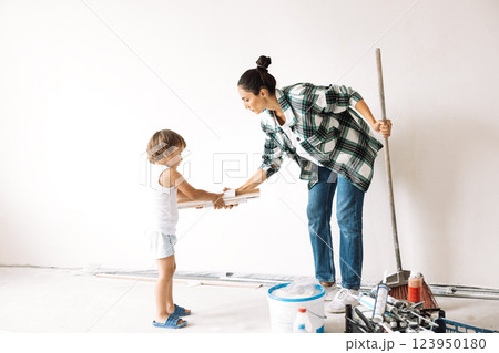 A little boy helps his mother clean the room. A young woman in casual clothes with a brush cleans the house. Mother sweeps the floor. Renovation of the apartment. A little boy helps his mother clean the room. A young woman in casual clothes with a brush cleans the house. Mother sweeps the floor. Renovation of the apartment. 123950180