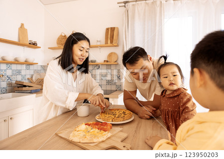 A happy Asian family is eating pizza in the kitchen at home A happy Asian family is eating pizza in the kitchen at home 123950203