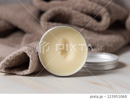 Opened body butter jar near light brown bath towel close up, herbal cosmetics for bodycare Opened body butter jar near light brown bath towel close up, herbal cosmetics for bodycare 123951068