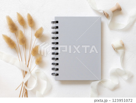 Blank spiral notebook on white plate near silk ribbons and hare's tail grass top view, mockup Blank spiral notebook on white plate near silk ribbons and hare's tail grass top view, mockup 123951072