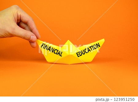 Financial education symbol. Concept words Financial education on beautiful yellow paper boat. Beautiful orange paper background. Businessman hand. Business Financial education concept. Copy space. Financial education symbol. Concept words Financial education on beautiful yellow paper boat. Beautiful orange paper background. Businessman hand. Business Financial education concept. Copy space. 123951250