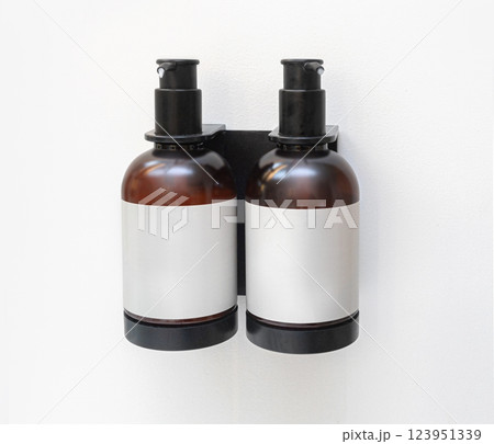 Two amber plastic bottles containing shampoo and conditioner hanging on wall 123951339