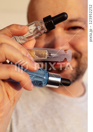 Close-up of a male hand with cosmetic bottles of serums. A young man is smiling and holding beauty products. Glass bottles with moisturizing vitamin essence. 123952252
