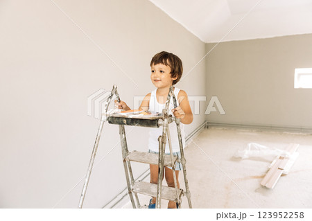 A little boy climbs on a stepladder in a renovated room. A laughing child is playing among the repairs in the house. A little boy climbs on a stepladder in a renovated room. A laughing child is playing among the repairs in the house. 123952258