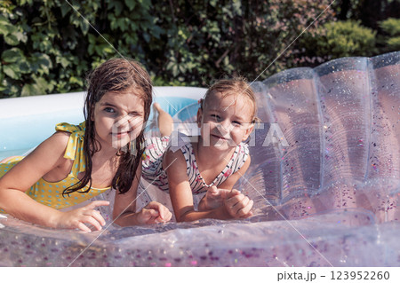 Two little carefree girls in swimsuits on an inflatable mattress. Cute friends have fun together in the pool on the terrace of the house. Two little carefree girls in swimsuits on an inflatable mattress. Cute friends have fun together in the pool on the terrace of the house. 123952260